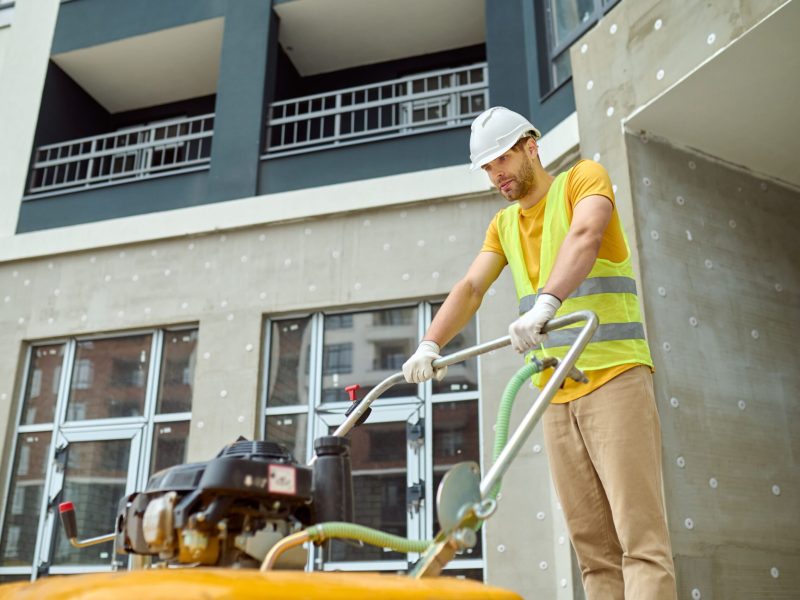 effort-fatigue-young-adult-tired-man-protective-helmet-bright-vest-with-special-equipment-working-construction-site-against-background-new-building-min